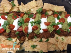 Nachos with beans, guacamole, sour cream, tomatoes and garnish on a serving tray